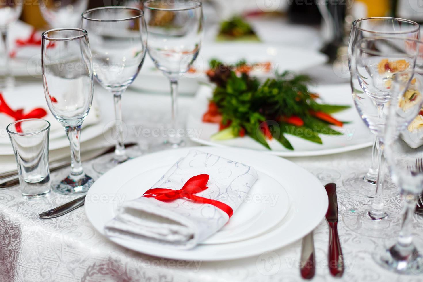 servilleta de mesa enrollada atada con cinta roja en un plato blanco vacío en la mesa. puesta de mesa, espacio libre. mesa servida para el banquete de bodas, vista de cerca foto