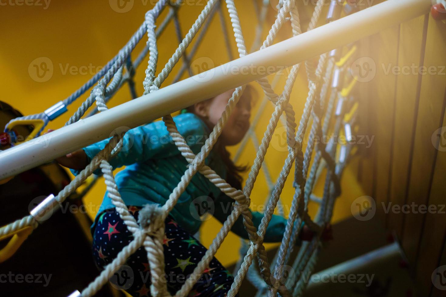 Active little child playing on climbing net and jumping on trampoline at school yard playground. Kids play and climb outdoors on sunny summer day. Cute girl on nest swing at preschool sport center. photo