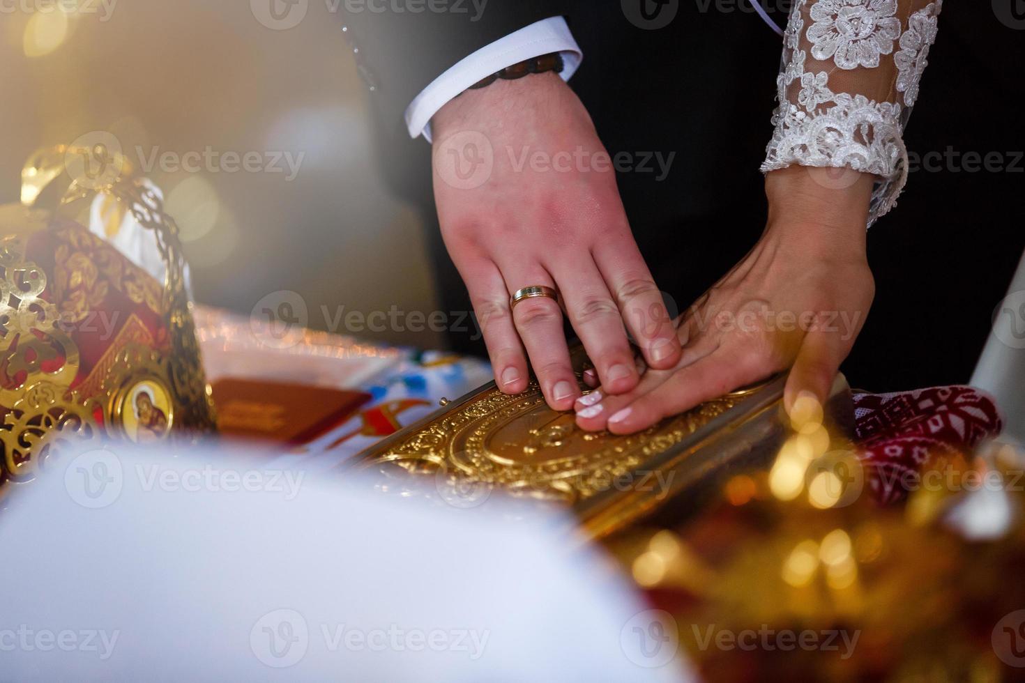 Newlyweds hold their hands on the golden Bible while standing on the knees photo