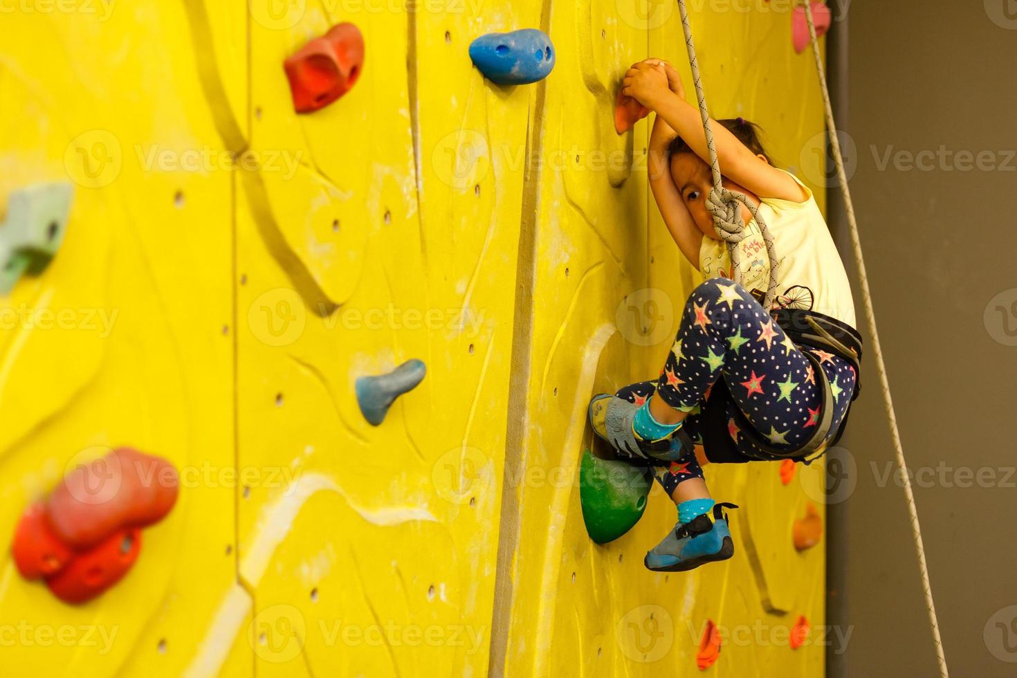 little girl climbing a rock wall indoor photo