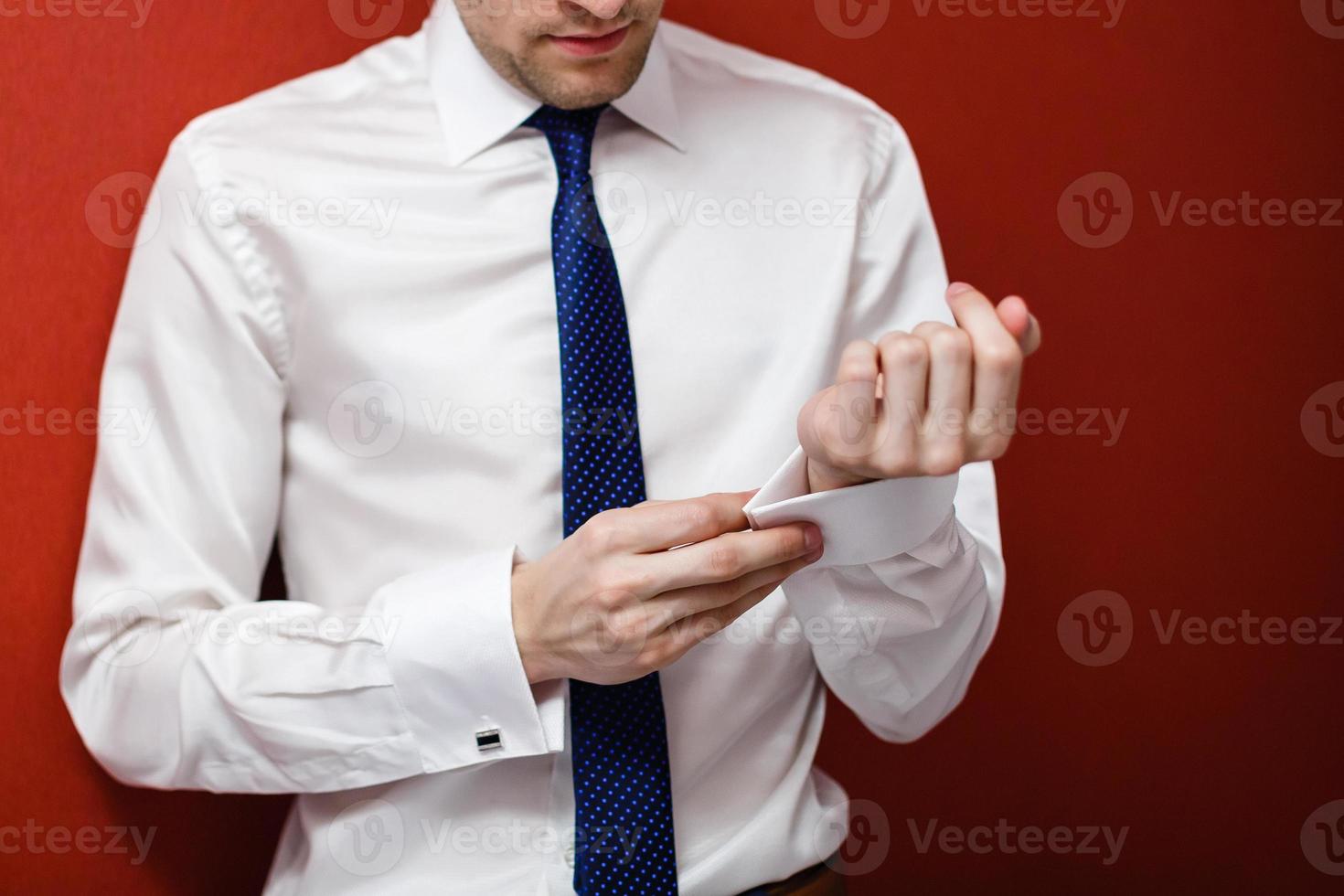 Man buttons up his white shirt standing in the front of a bright window photo