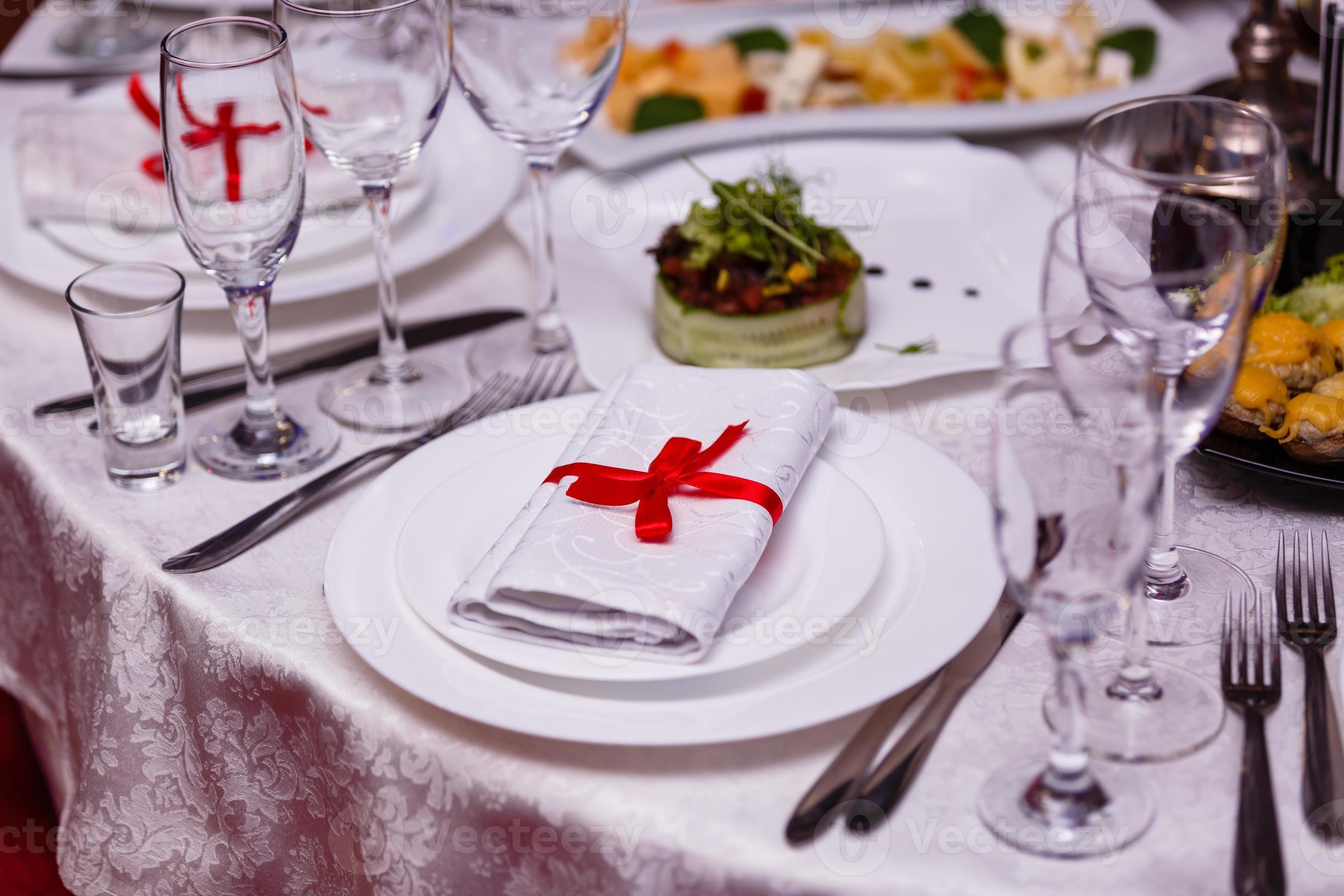 napkin tied with red ribbon on white empty plate on table. Table served
