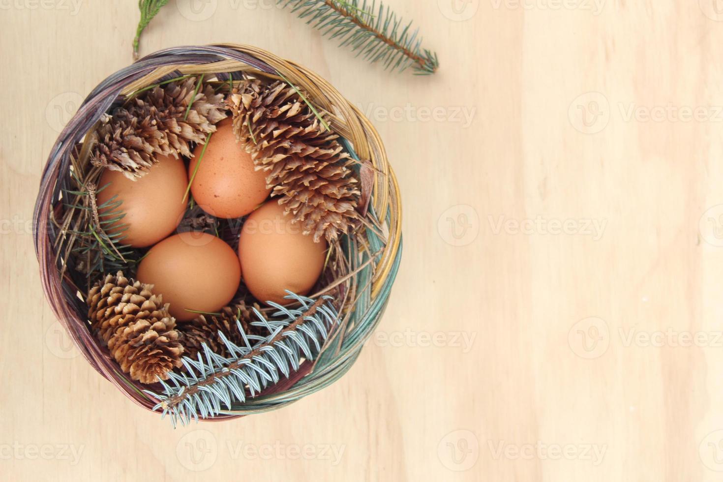 Easter eggs in a basket of 4 with pine leaves and pine cones on a light wooden background. photo