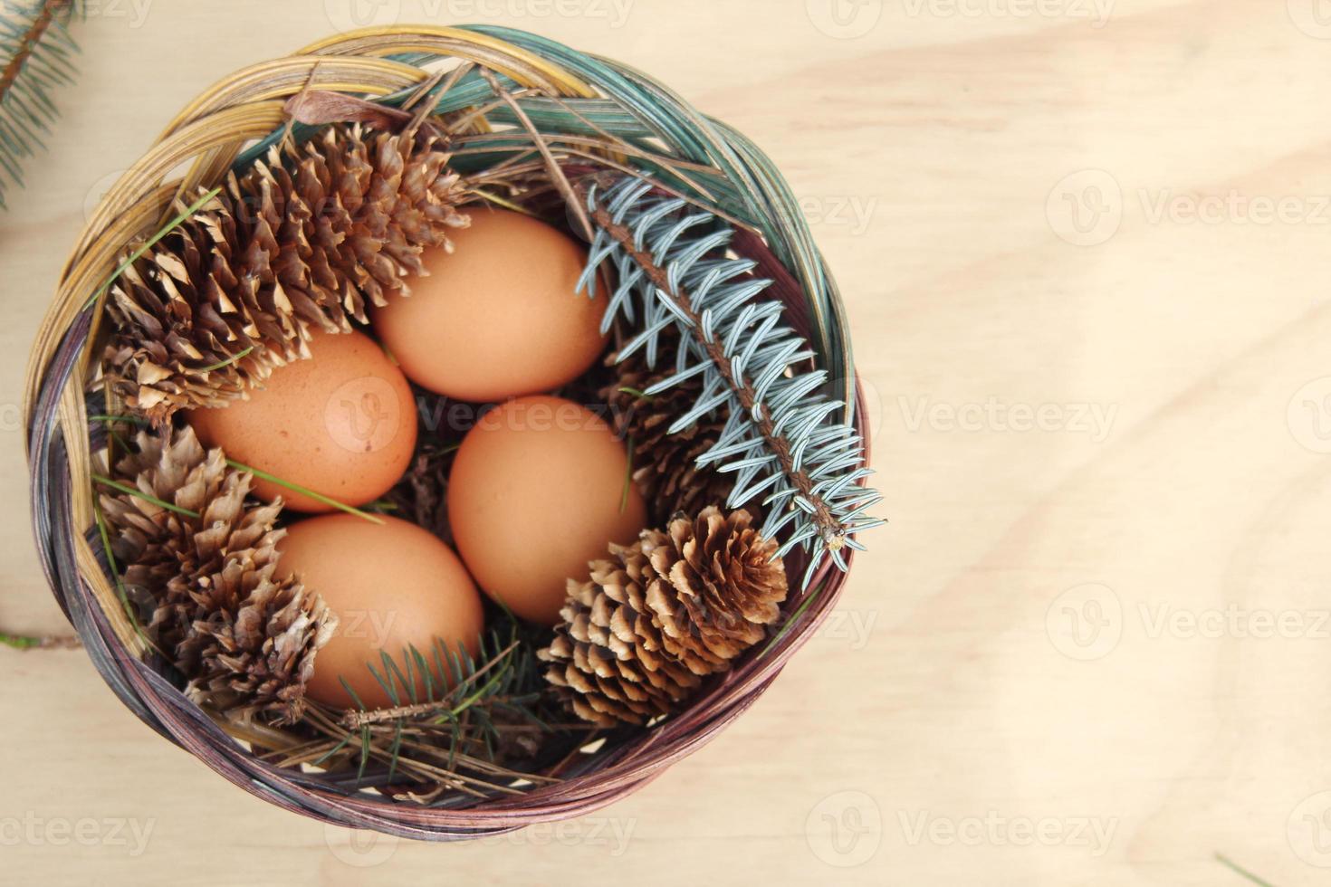 Easter eggs in a basket of 4 with pine leaves and pine cones on a light wooden background. photo