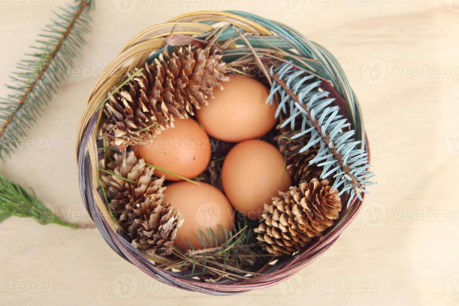 Easter eggs in a basket of 4 with pine leaves and pine cones on a light wooden background. photo