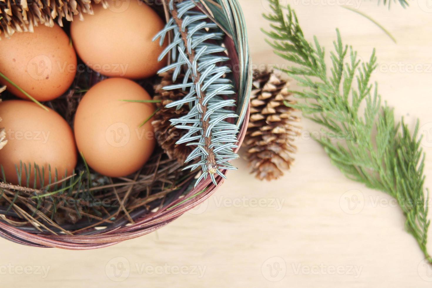 Easter eggs in a basket of 4 with pine leaves and pine cones on a light wooden background. photo