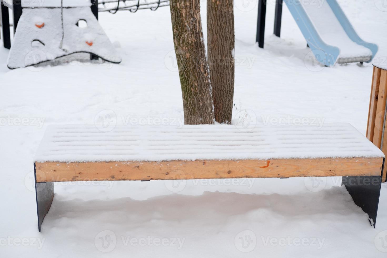 banco vacío cubierto de nieve en la calle, en el patio de recreo foto