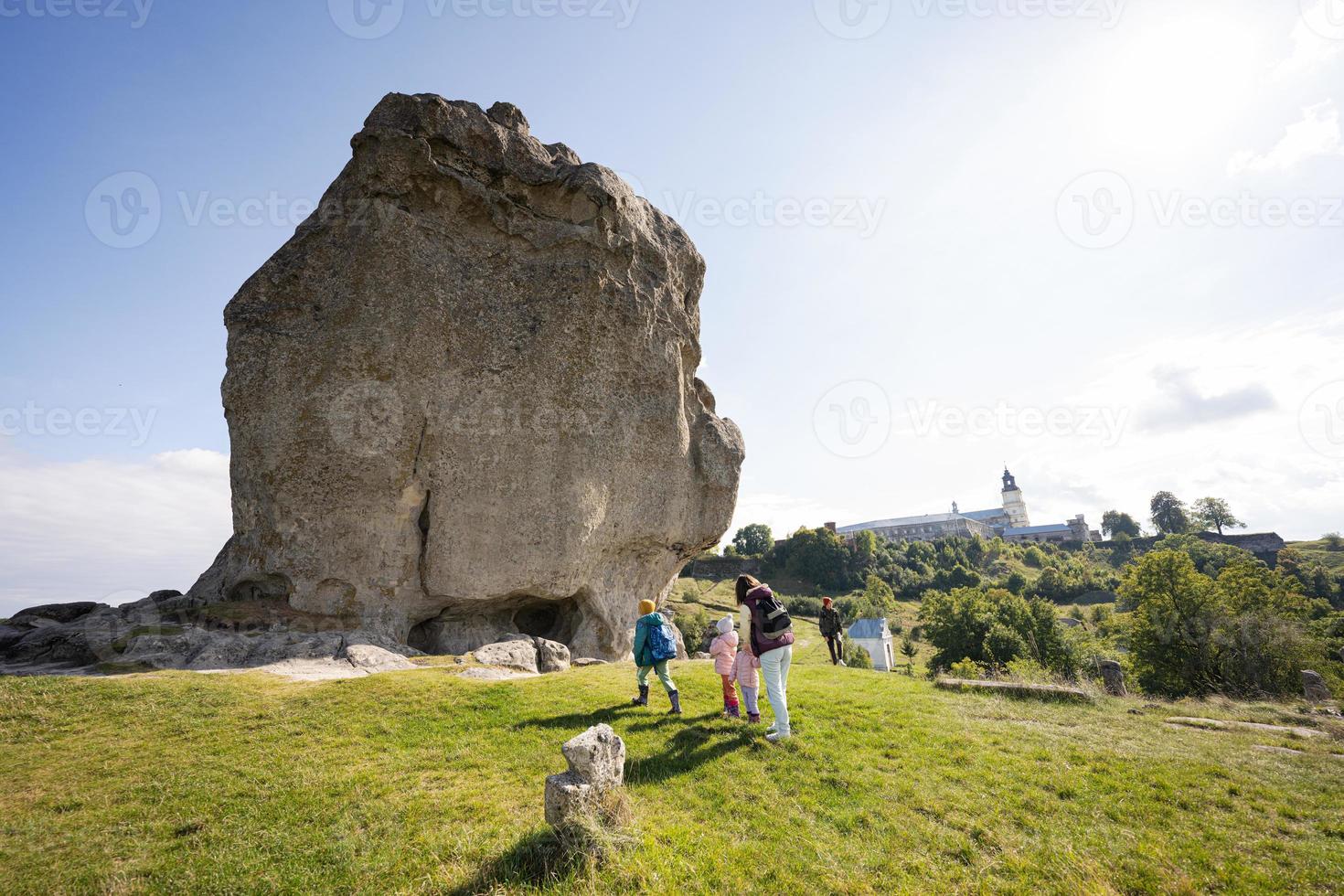 Kids exploring nature. Children wear backpack hiking with mother near big stone in hill. Pidkamin, Ukraine. photo