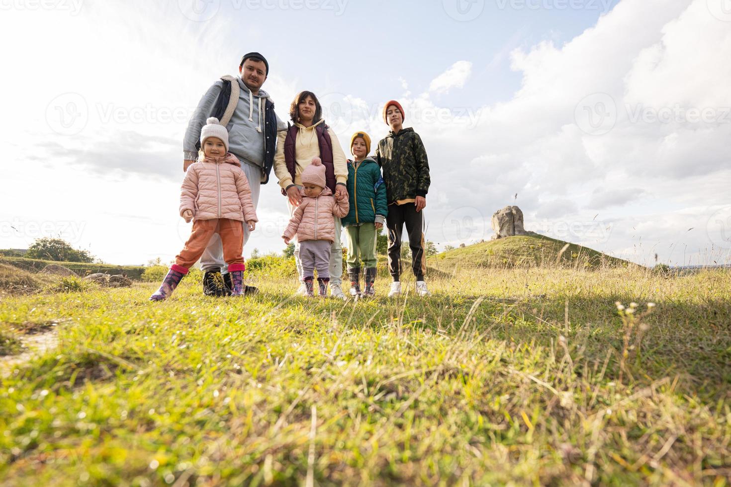 familia explorando la naturaleza. los niños con padres se paran contra una gran piedra en la colina. pidkamin, ucrania. foto