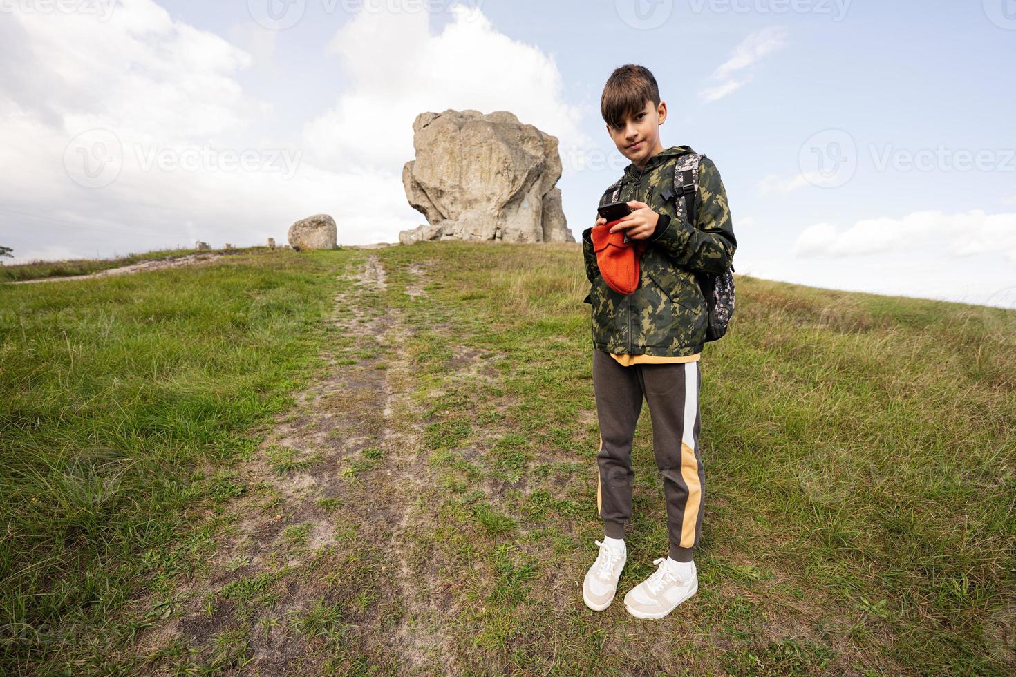 Activity on sunny autumn day, boy exploring nature. Kid wear backpack hiking and making photo on phone.