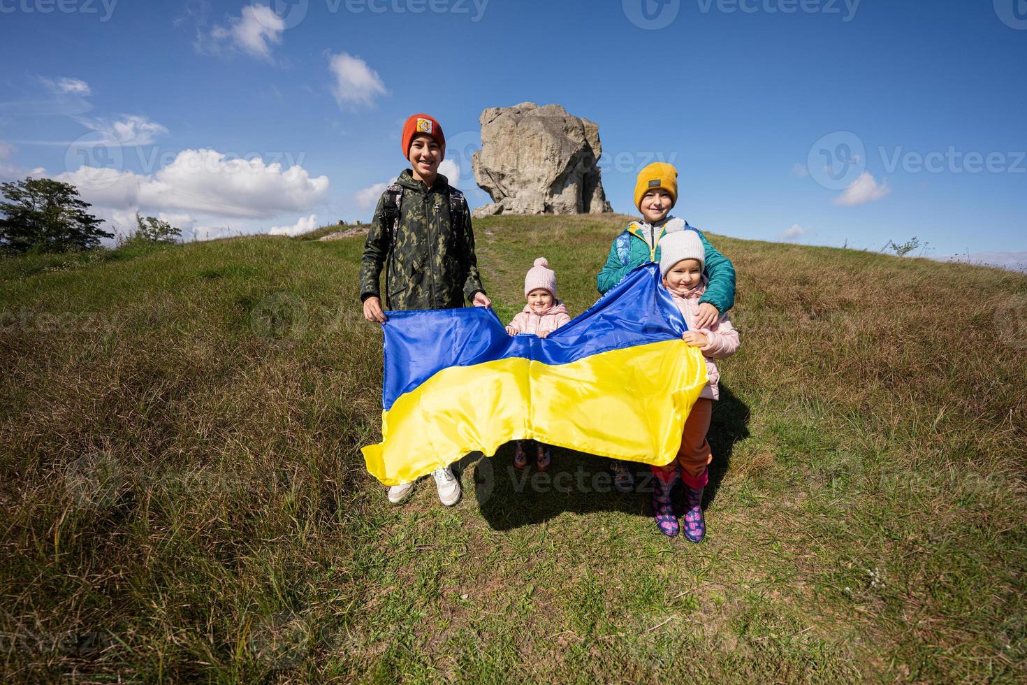 Welcome to Ukraine. Four children hold ukrainian flag near big stone in hill Pidkamin. photo