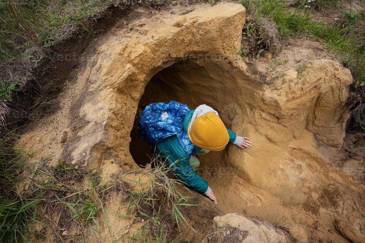 Boy with backpack explore limestone stone cave at mountain. photo