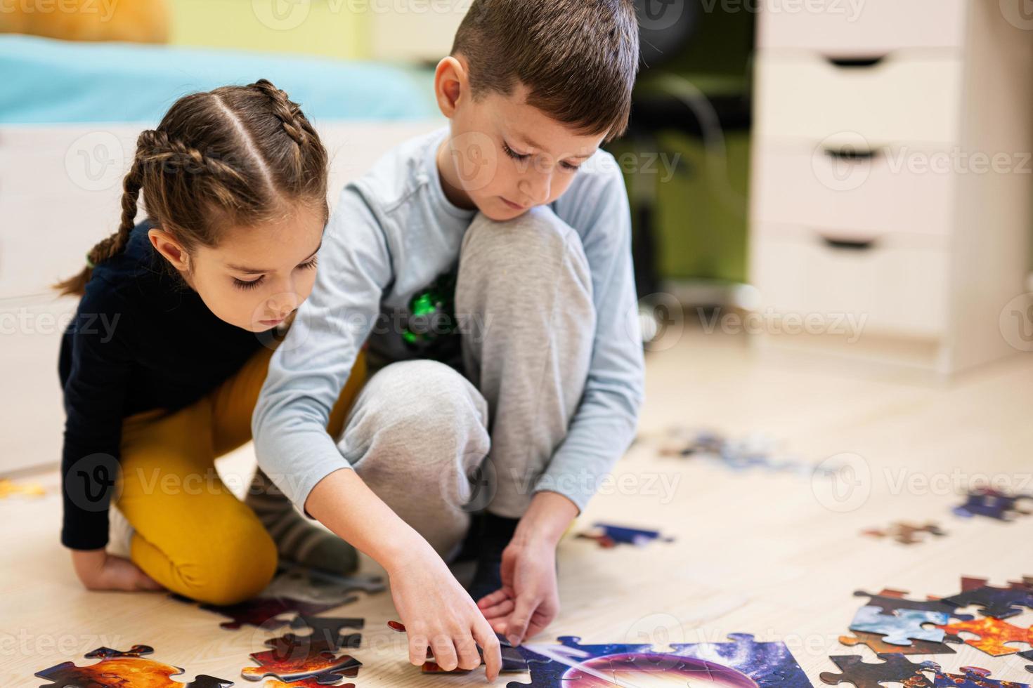 niños conectando piezas de rompecabezas en una habitación para niños en el piso en casa. diversión actividad familiar ocio. foto