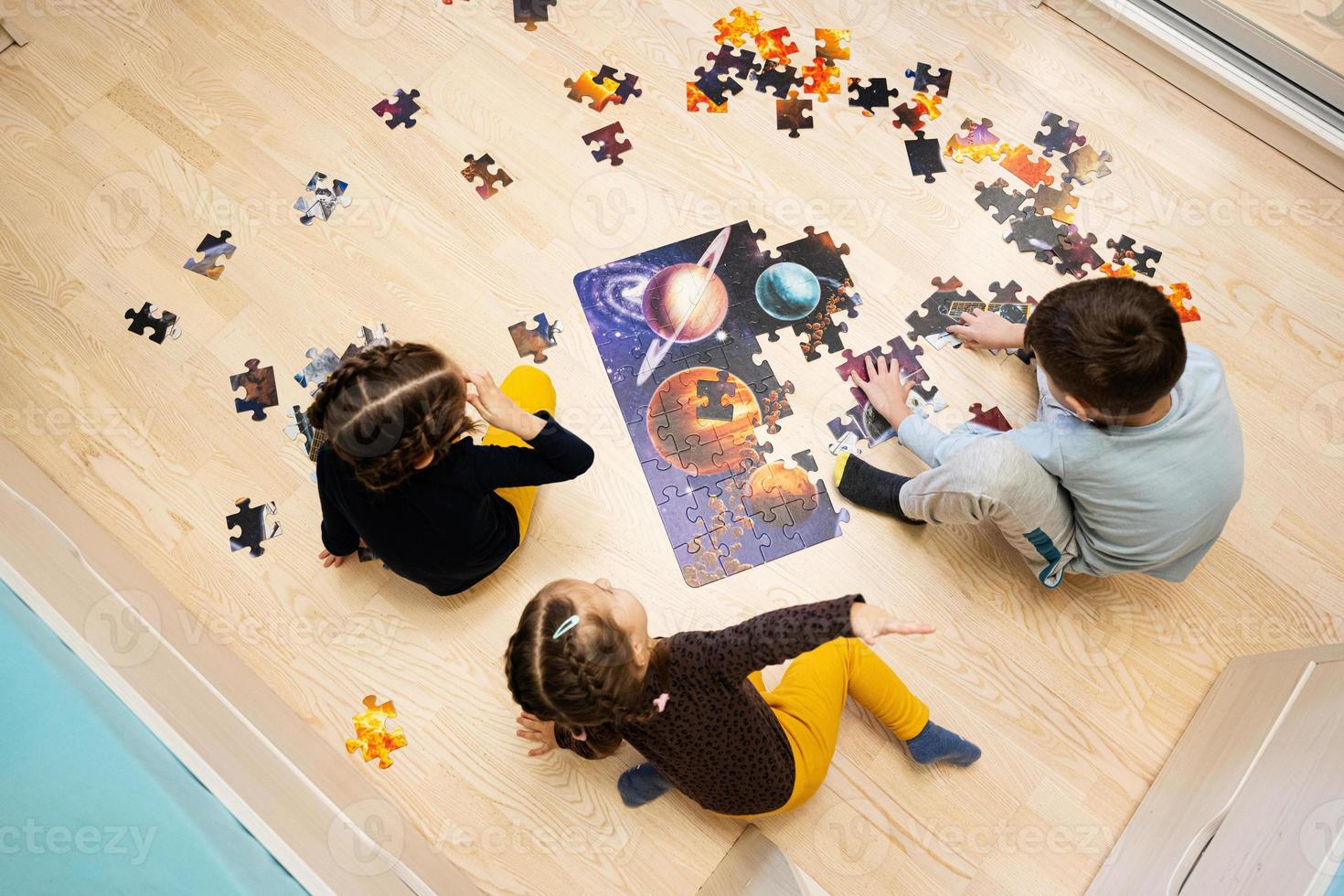 niños conectando piezas de rompecabezas en una habitación para niños en el piso en casa. diversión actividad familiar ocio. foto