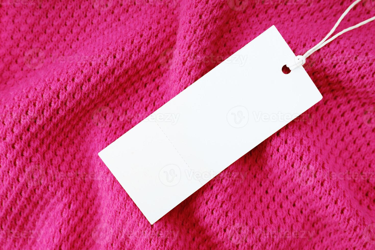 White blank rectangular clothing tag on pink knitted fabric background. Shopping, sale, discount mockup photo