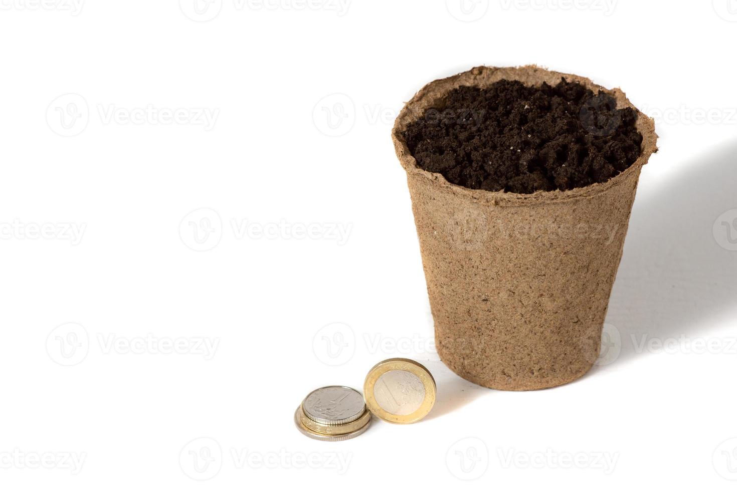 Coin and a peat pot for seedlings lying together, in a rural agricultural production company isolated over white. photo