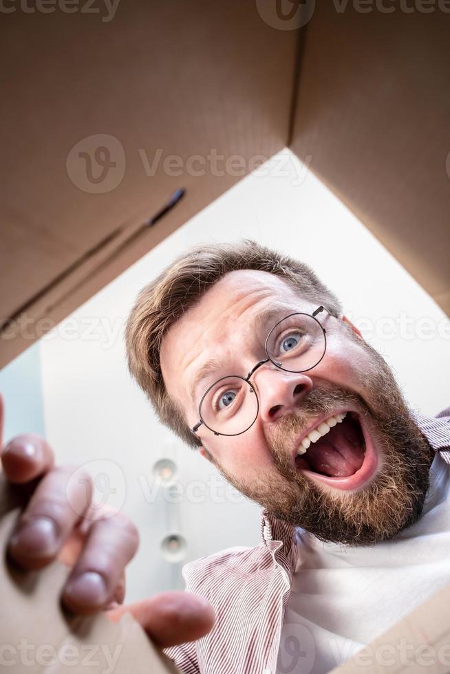 Happy man unpacks the delivered box with the parcel. Unpacking inside view. photo