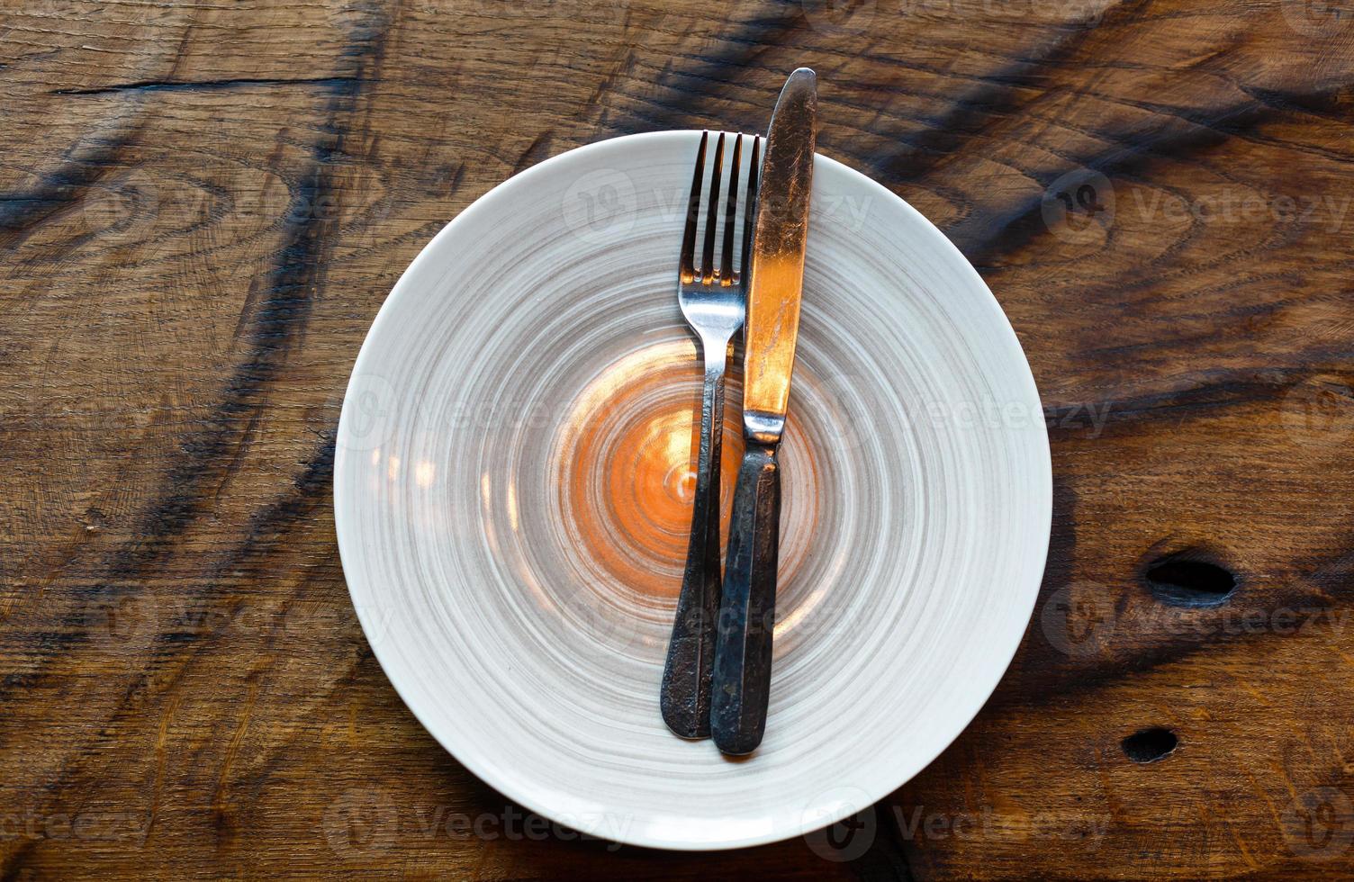 Empty plate with knife and fork on vintage wooden table photo