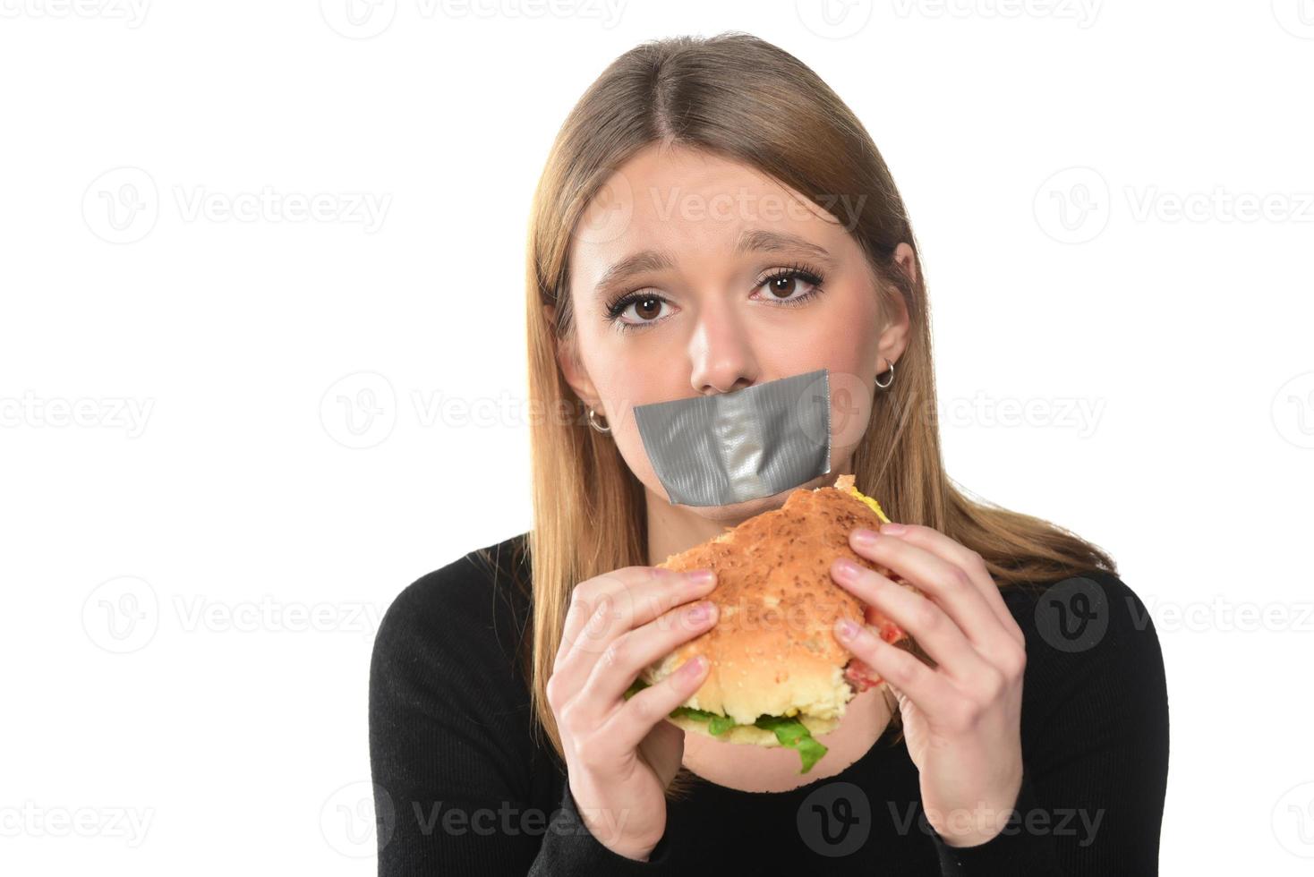 portrait of a beautiful funny young girl with tape over her mouth on the white background, blonde holding a tray with hamburger photo