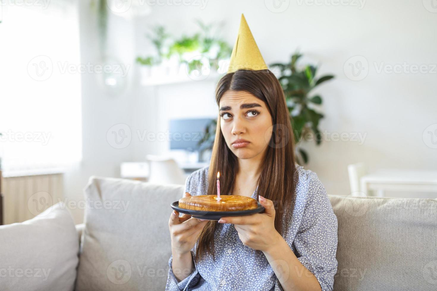 Virtual Party During Lockdown. Upset and frustrated single african american woman in party hat celebrating birthday online. Lady making video conference, holding cake with candle, sitting on the floor photo