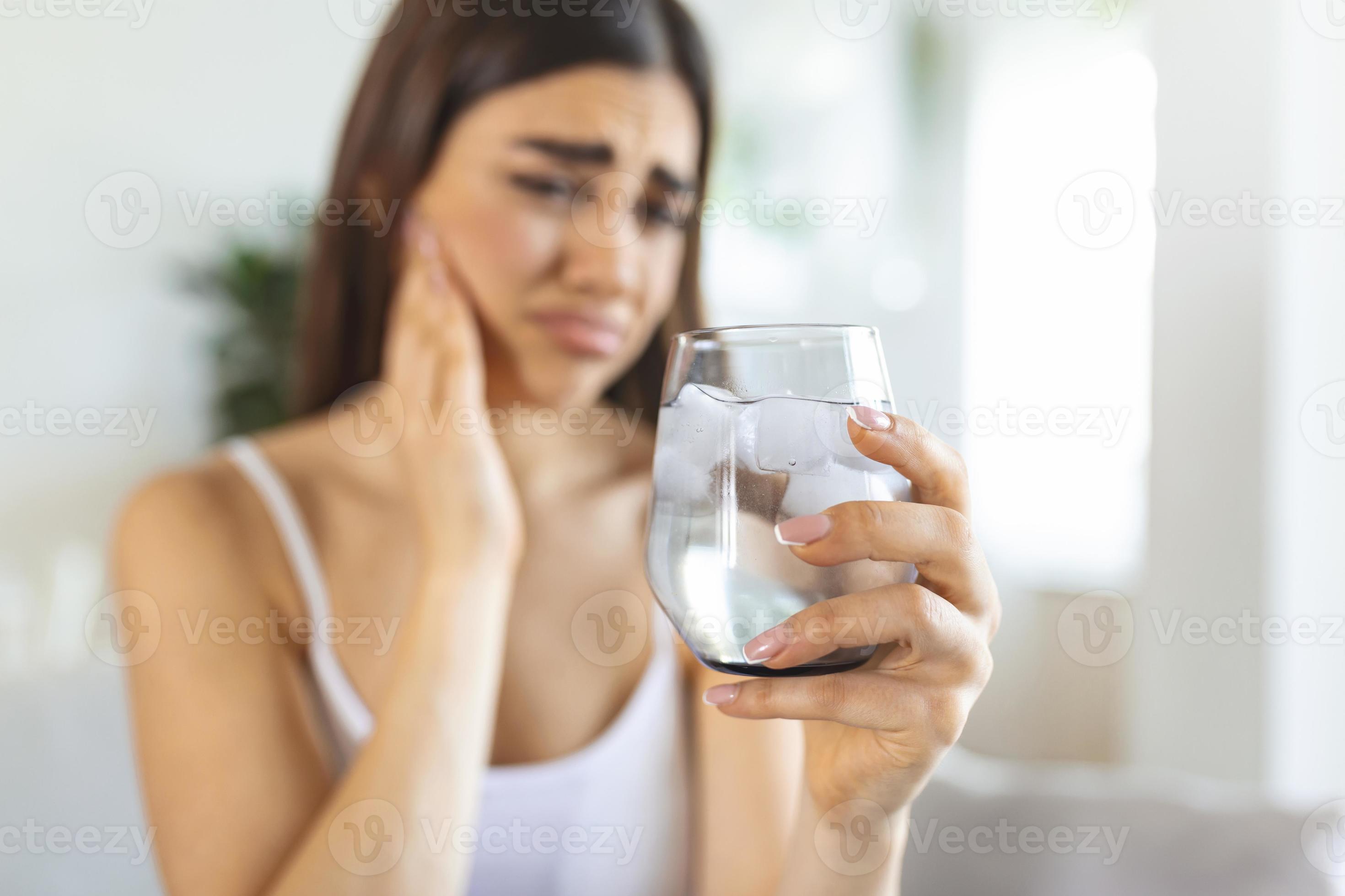 Young woman with sensitive teeth and hand holding glass of cold water