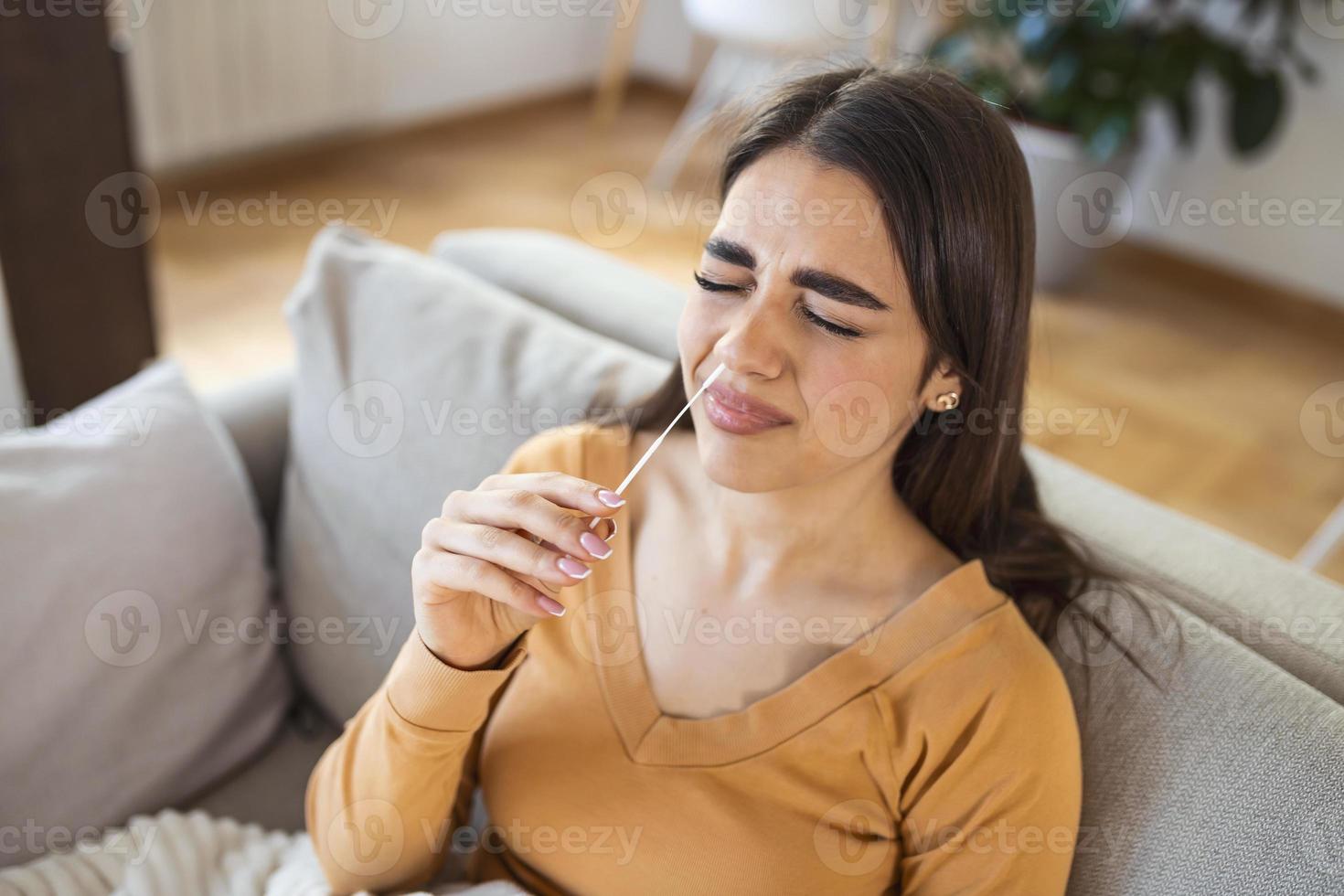 woman using cotton swab while doing coronavirus PCR test at home. Woman using coronavirus rapid diagnostic test. Young woman at home using a nasal swab for COVID-19. photo