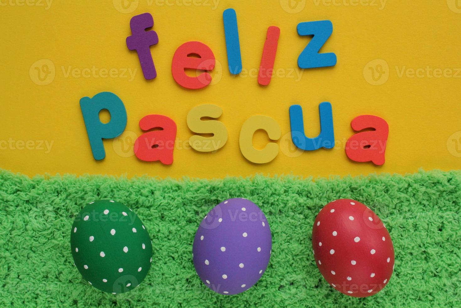 Feliz Pascua, Happy Easter letters on spanish on yellow background and color eggs on green grass. Holiday banner, flatlay creative composition. Greeting card, poster, banner. Top view festive concept photo