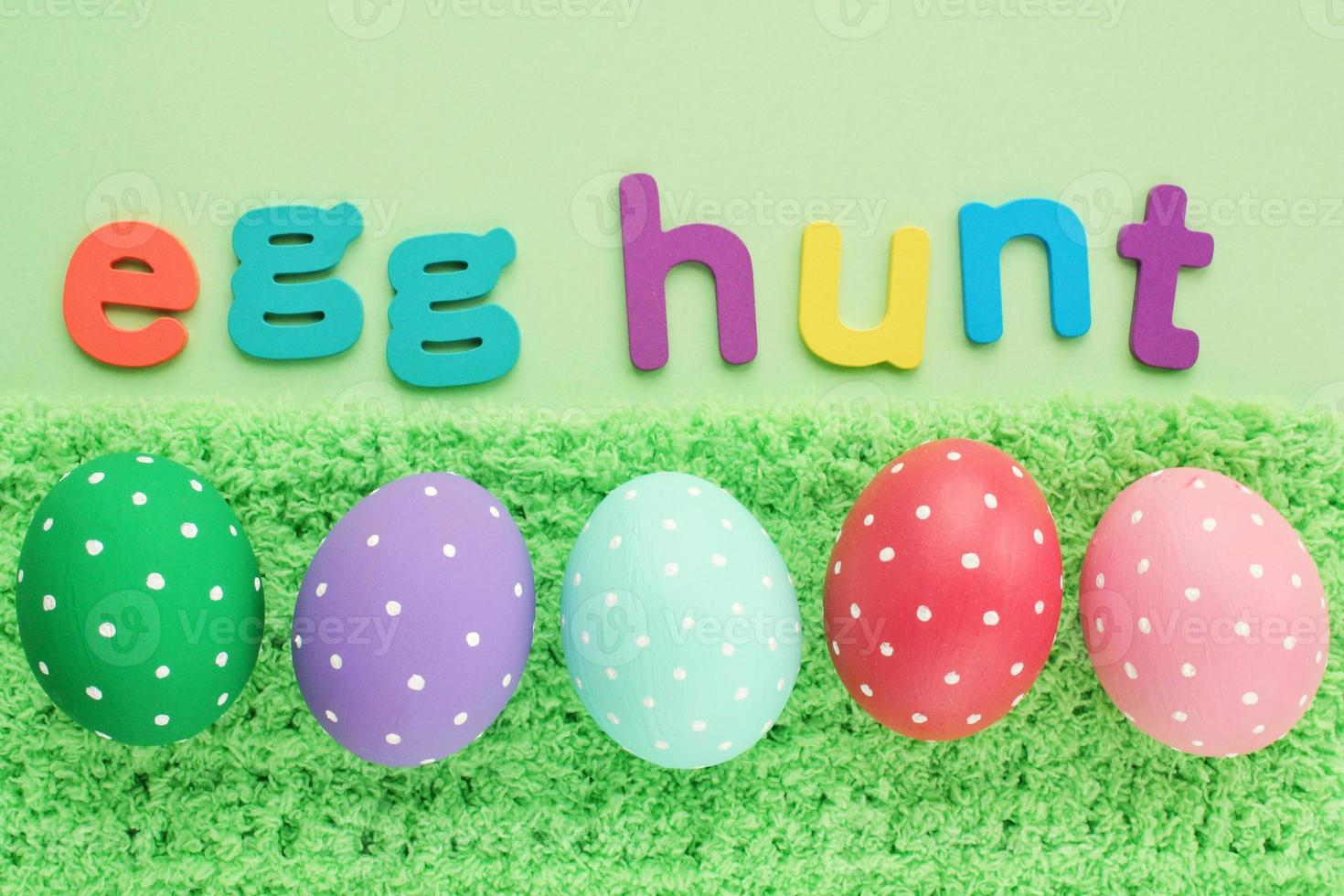 Egg hunt letters on green background and coloured eggs with polka dot on spring grass background. Easter greeting card, invitation, banner, poster sale. Flatlay, top view holiday concept. Sign for fun photo