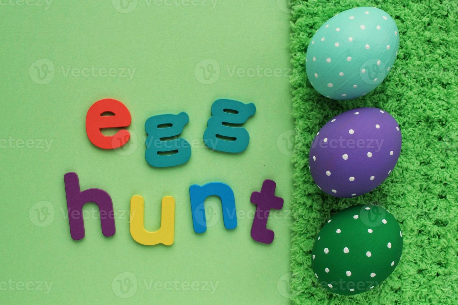 Egg hunt letters on green background and coloured eggs with polka dot on spring grass background. Easter greeting card, invitation, banner, poster sale. Flatlay, top view holiday concept. Sign for fun photo