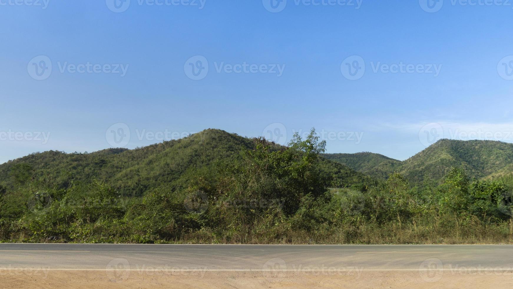 Horizontal view of asphalt road in Thailand. Background of green forest and mountain under the blue sky. photo