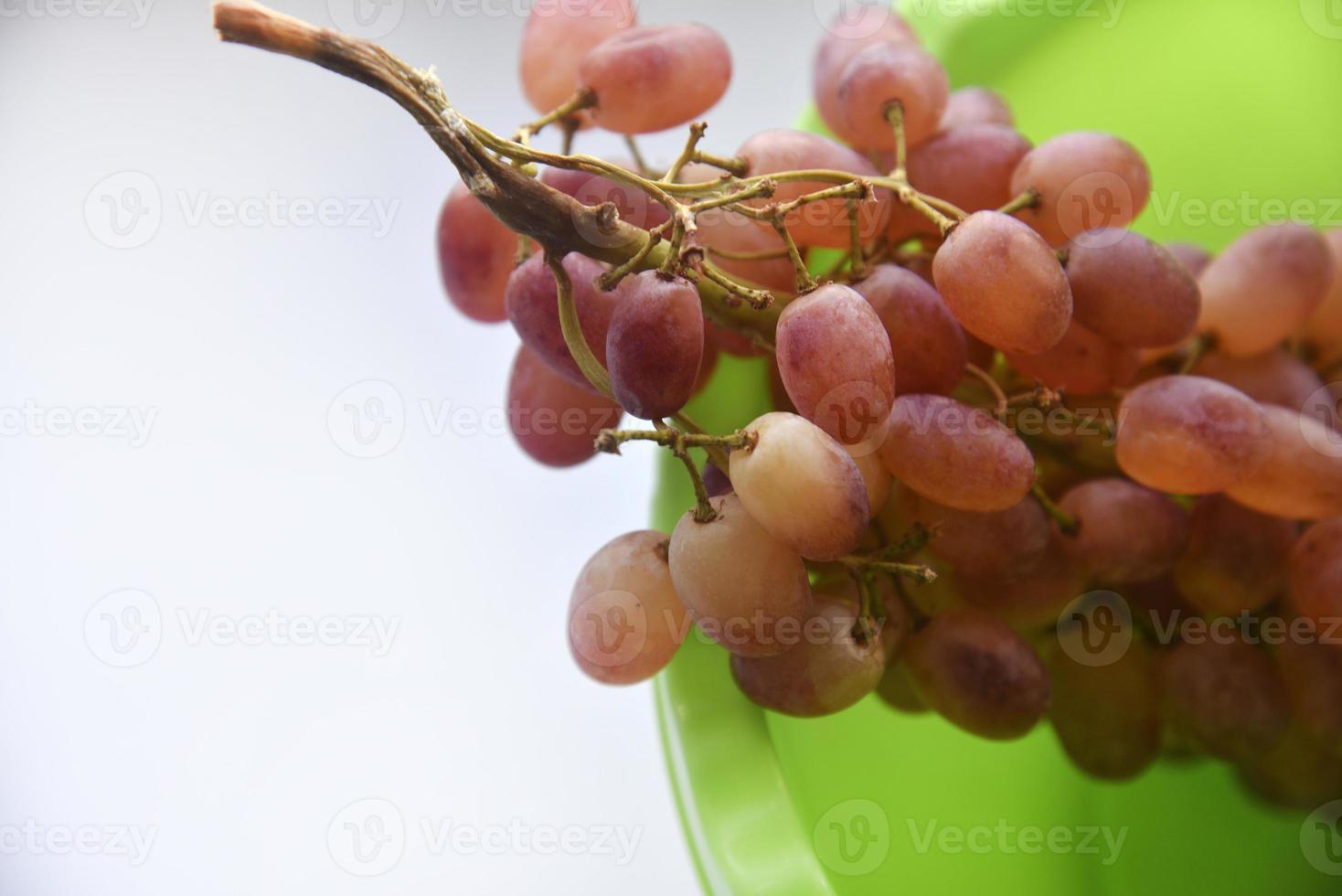 A branch of red grapes on a green plate. Washed grapes in a plastic container. photo