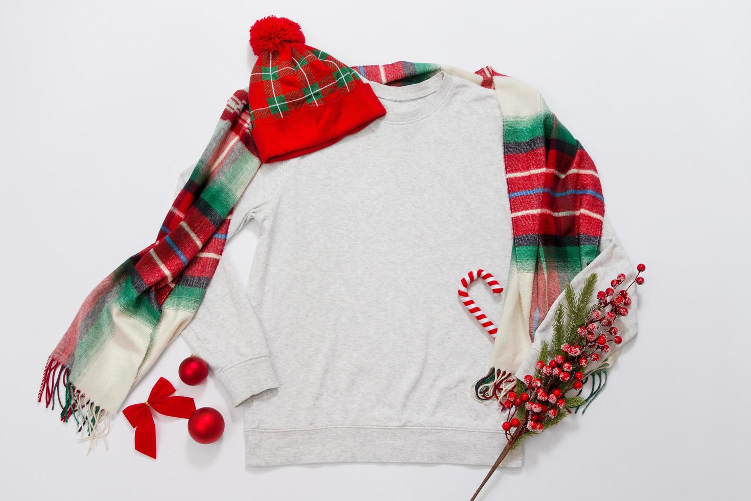 Close up grey blank template sweatshirt copy space. Christmas Holiday concept. Top view mockup hoodie, scarf, hat. Red holidays decorations on white background. Happy New Year accessories. Xmas outfit photo