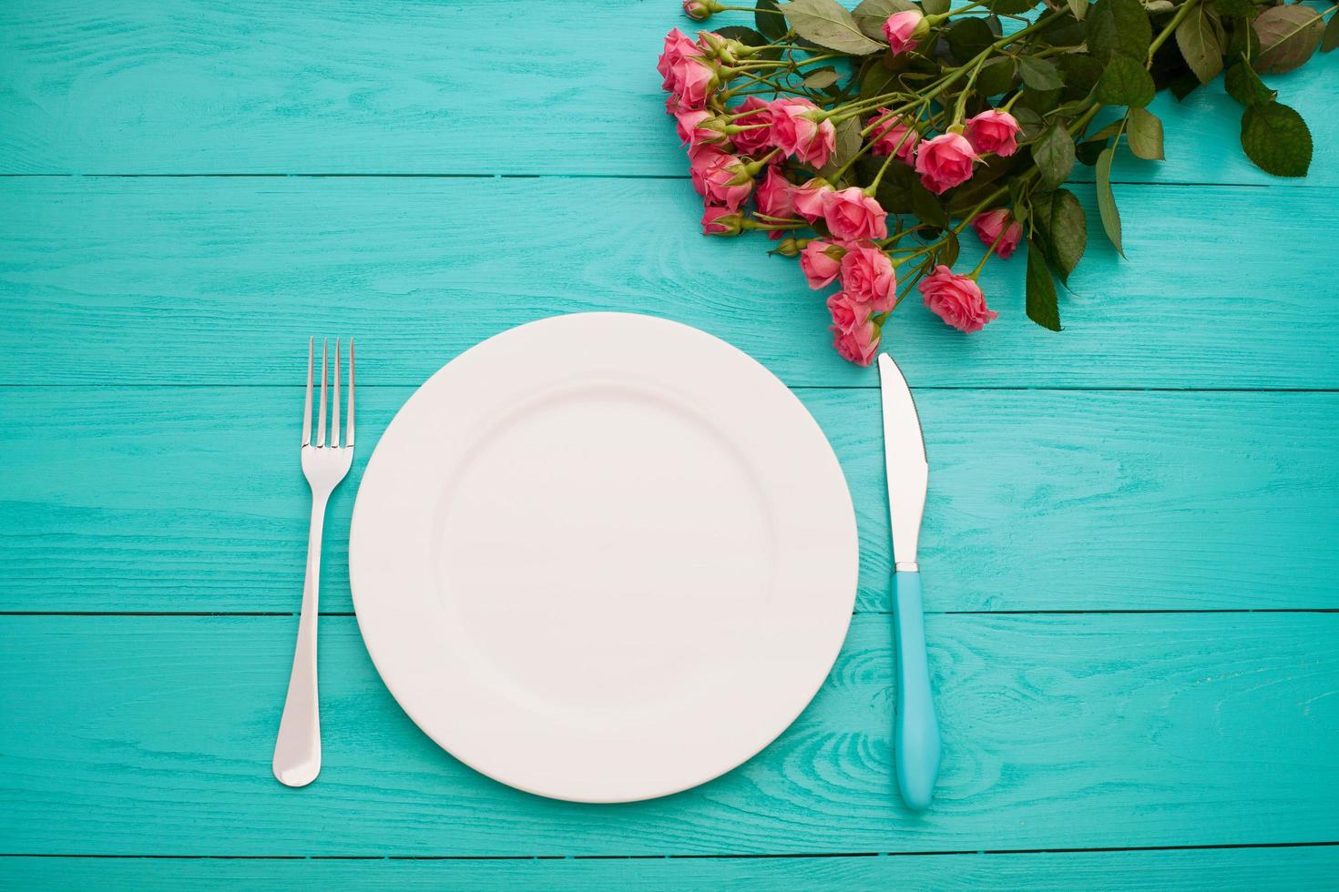 Top view of tableware of round and heart shaped empty plate, metal knife and fork served on white wooden table with glowing candle and gift box prepared for celebration of saint valentine day photo