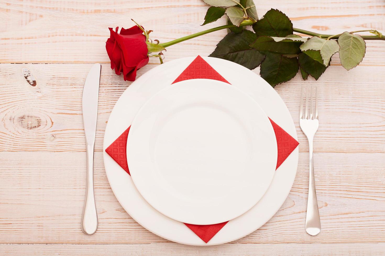 Top view of tableware of round and heart shaped empty plate, metal knife and fork served on white wooden table with glowing candle and gift box prepared for celebration of saint valentine day photo