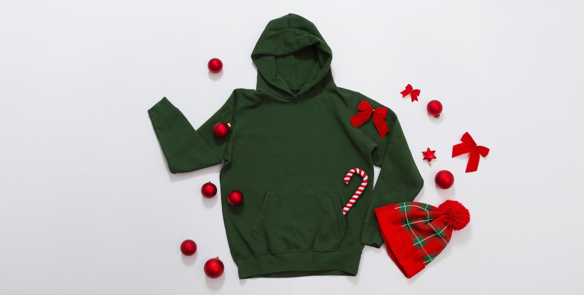 Close up banner green blank template hoodie copy space. Christmas Holiday concept. Top view mockup hoodie. Red holidays decorations on jumper white background. Happy New Year accessories. Xmas photo