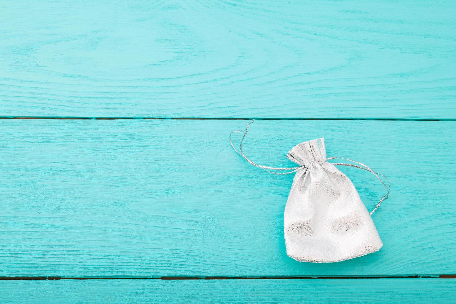 White silver drawstring bag on blue wooden background. Fabric cotton small bag. Jewelry pouch. Top view. Copy space and mock up. photo