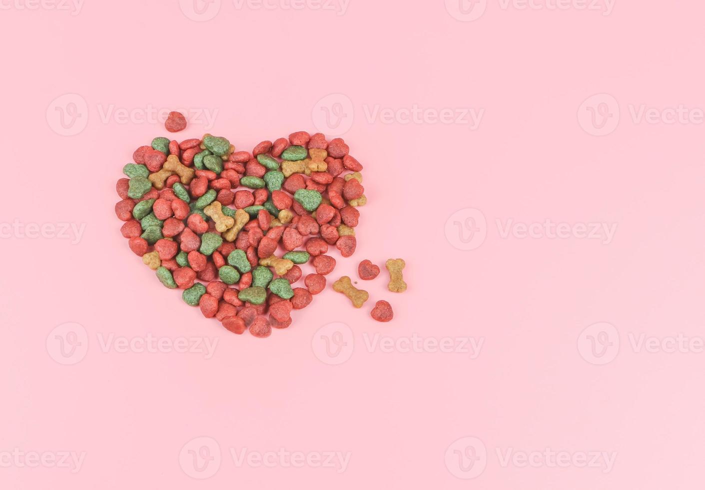 endecha plana de comida seca para perros en forma de corazón sobre fondo rosa. concepto de amante de los perros y el día de san valentín. foto