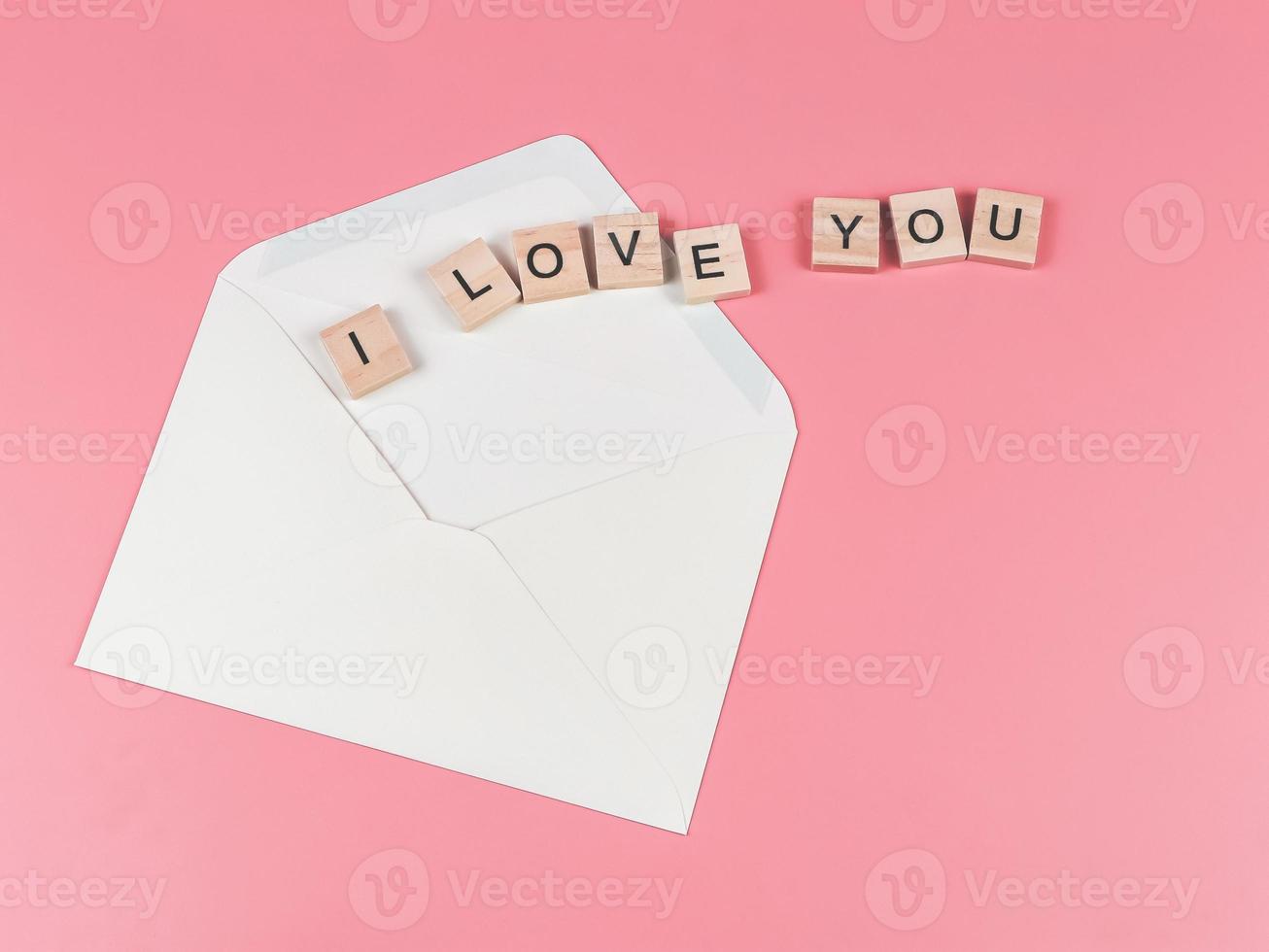 flat lay of wooden letter I love you out of the envelope on pink background. photo