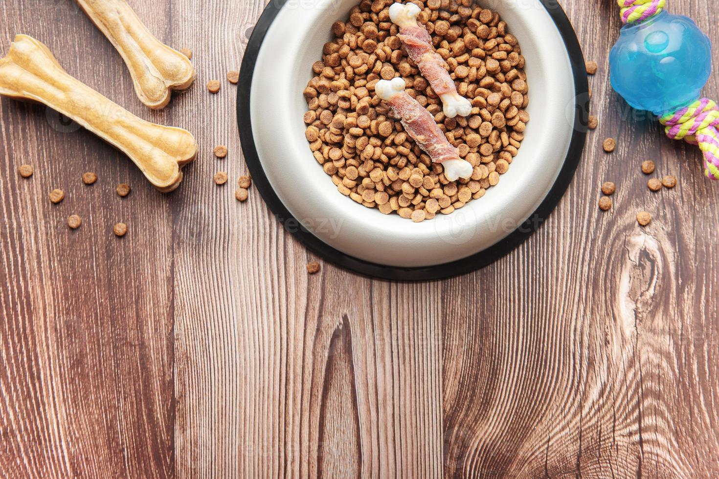 un tazón con comida para perros, golosinas para perros y juguetes en un piso de madera. foto