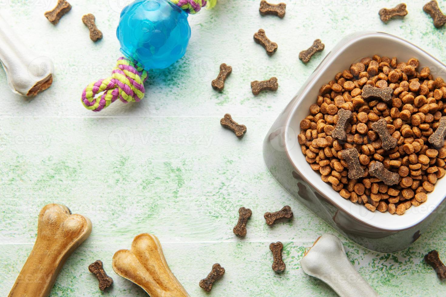 A bowl with dog food, dog treats and toys on a wooden floor. photo