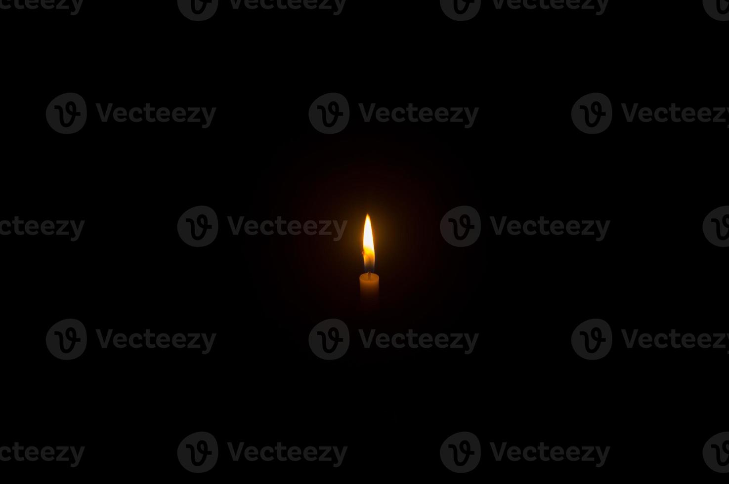 Small burning candle flame or light glowing on a white candle on black or dark background on table in church for Christmas, funeral or memorial service with copy space photo