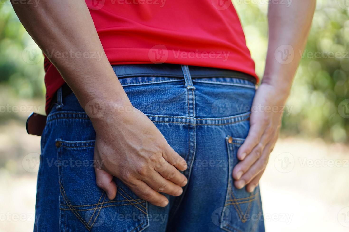 el hombre de primer plano usa jeans, usa sus manos para tocar el fondo, se siente herido. concepto, tener hemorroides, diarrea, dolor en el trasero por estar mucho tiempo sentado, problema de salud, atención médica. foto