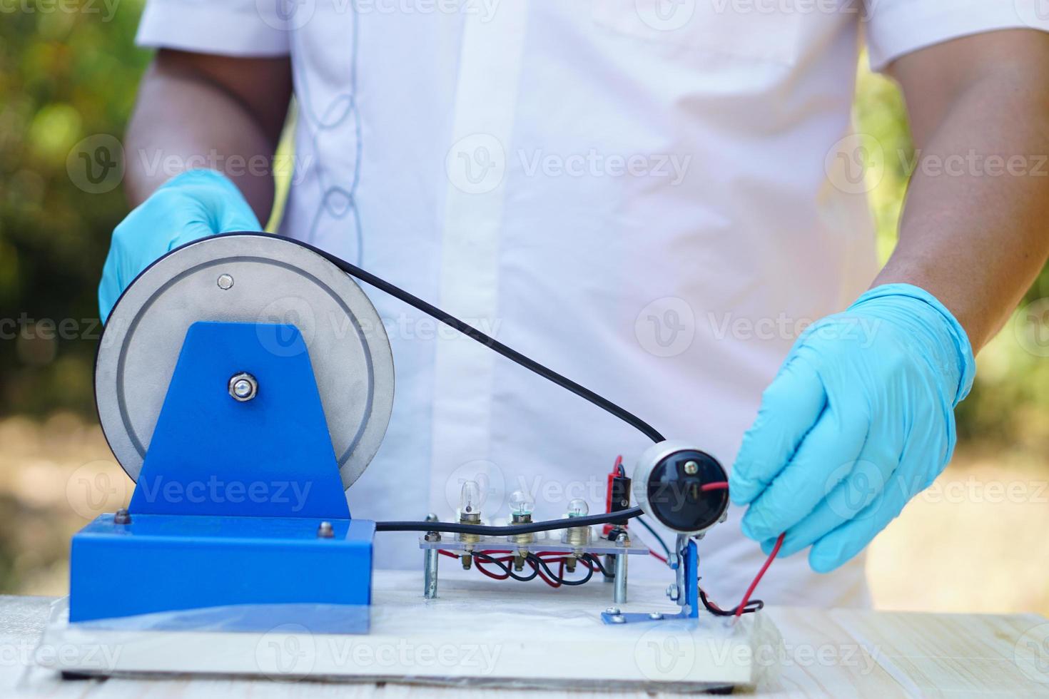 Close Up hands wear blue gloves demonstrate science experiment about electricity circuit from dynamo kit for teaching. Concept, science subject, project work. Experiment, education. Outdoor class. photo