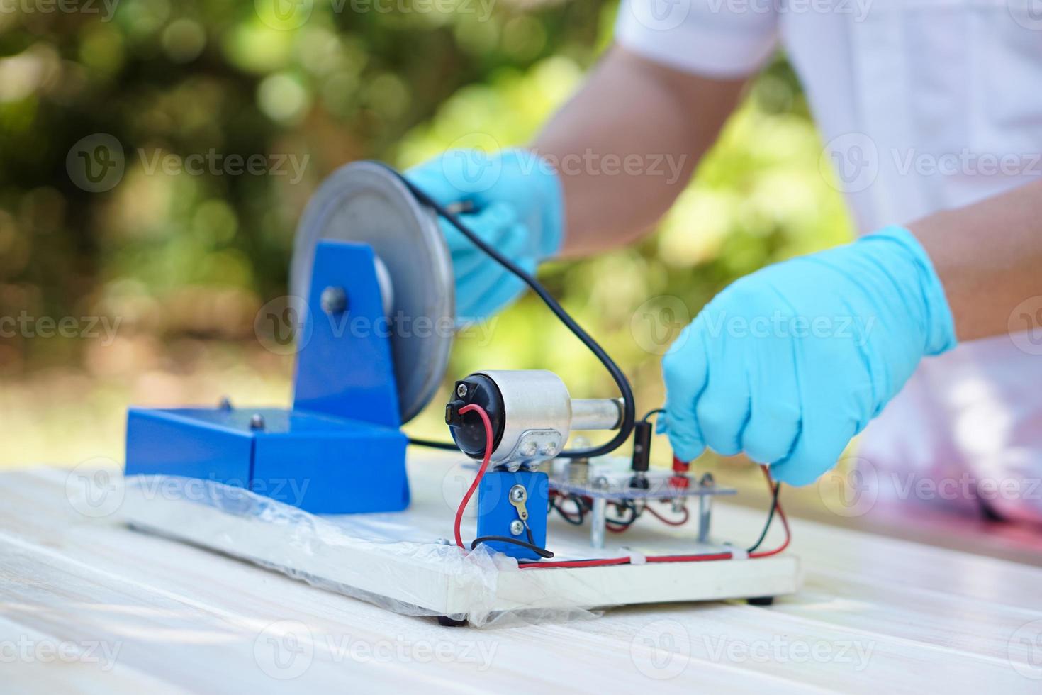 Close Up hands wear blue gloves demonstrate science experiment about electricity circuit from dynamo kit for teaching. Concept, science subject, project work. Experiment, education. Outdoor class. photo