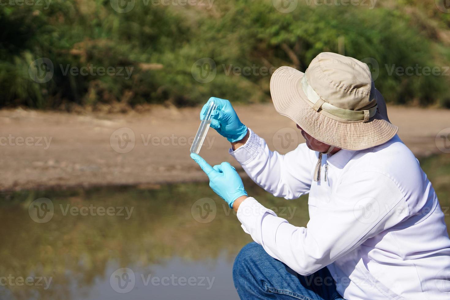 Asian man environment researcher holds tube of sample water to inspect at the lake. Concept, explore, analysis water quality from natural source. Ecology field research. photo