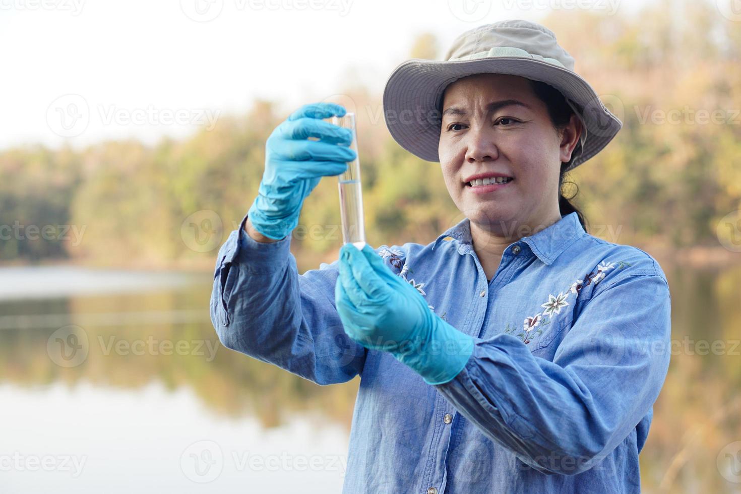 Asian women environment researcher holds tube of sample water to inspect at the lake. Concept, explore, analysis water quality from natural source. Ecology field research. photo