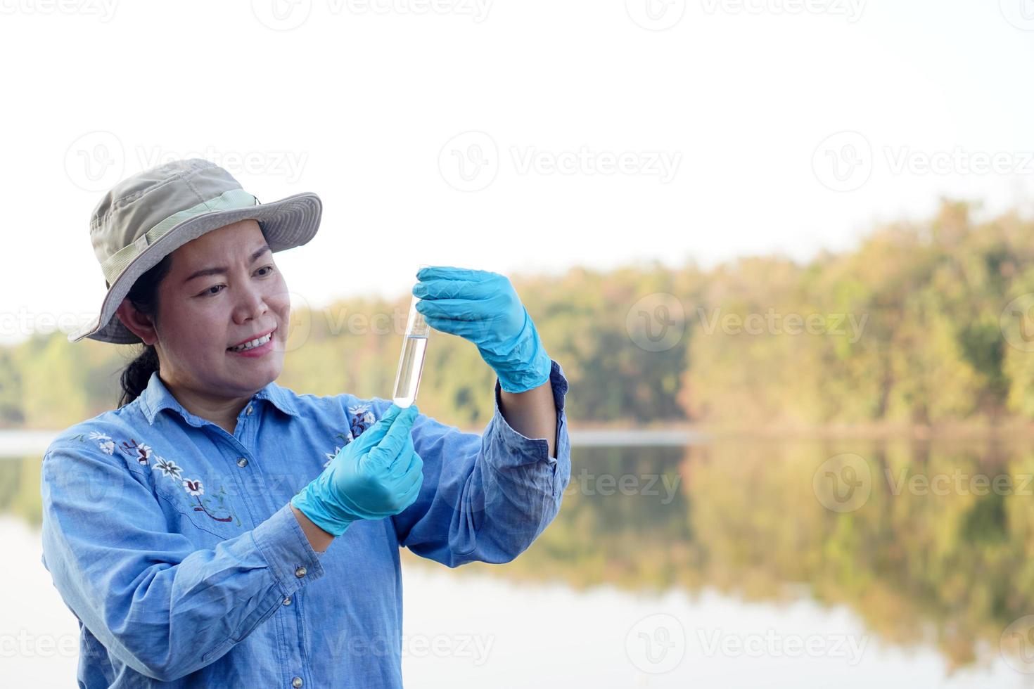 una investigadora ambiental asiática sostiene un tubo de agua de muestra para inspeccionar desde el lago. concepto, exploración, análisis de la calidad del agua de fuente natural. Investigación de campo en ecología. foto