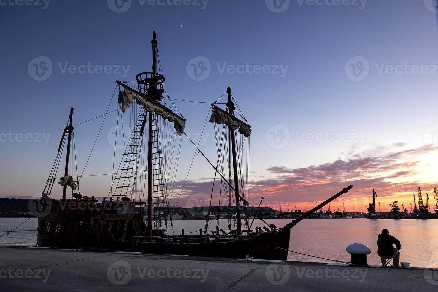 Silhouette photo of sailing ship moored in the port and fisherman in the evening