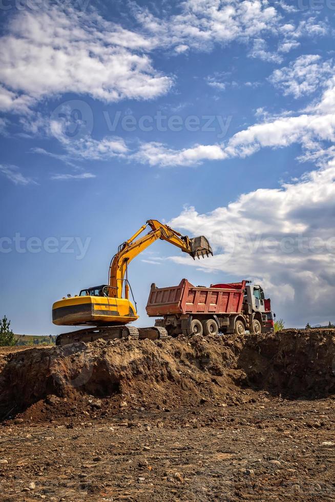 Yellow excavator and empty dump truck working at the construction site. Vertical view photo