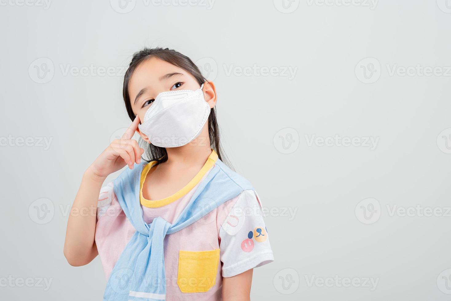 Asian little child girl wearing respirator mask to protect coronavirus outbreak and pointing hand to blank background, New virus Covid-19 photo